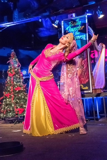 Erin McGurk performing a Middle Eastern dance on stage in a magenta and gold gown