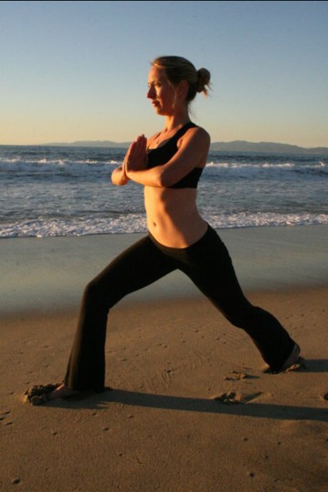 Erin McGurk holding a standing yoga pose with hands at her heart on the beach