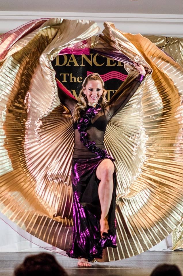 Erin McGurk performing on stage with large gold fan wings